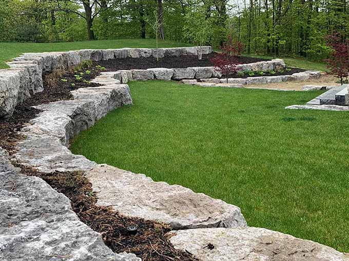 Backyard with armour stone retaining wall and greenery by Greenblock.