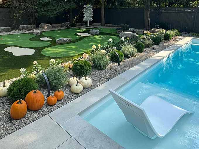 Backyard with putting green and pool by Greenblock Landscape