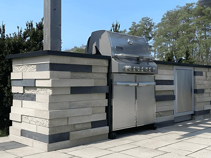 Outdoor kitchen with stone veneer and stainless grill on interlock patio