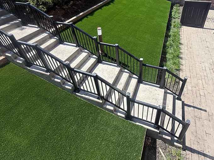 Concrete steps leading down to a green turf area in a landscaped yard.