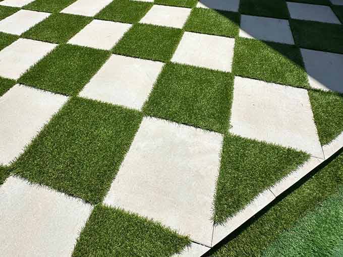 Patio with alternating pavers and artificial turf in a checkerboard pattern.