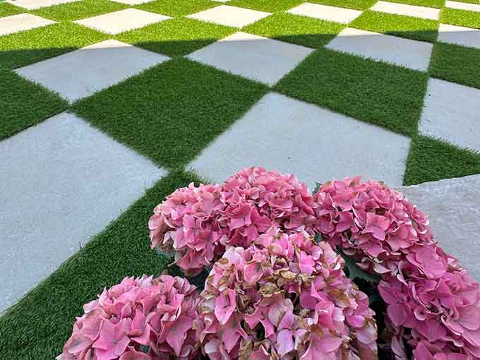 Patio with checkerboard paver and turf design, pink flowers.