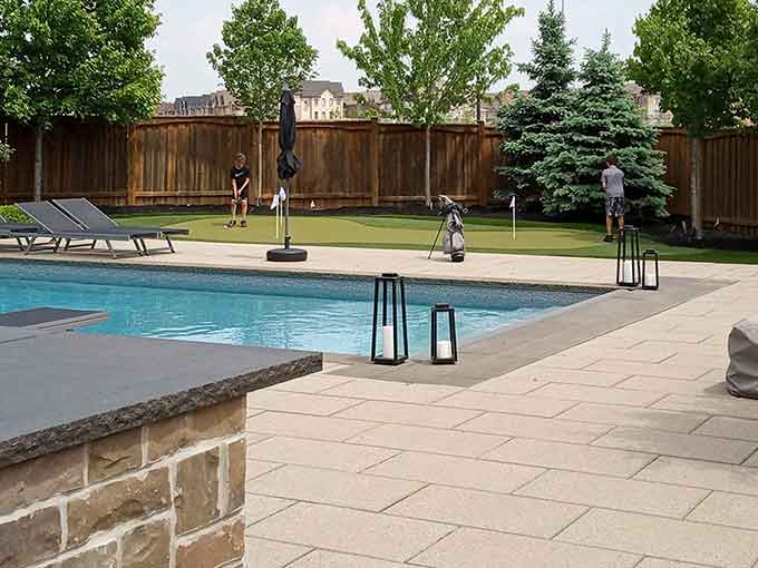 A backyard with a pool, patio, and a putting green.