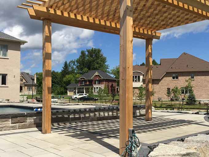Patio with wooden pergola, pool, and landscaped gardens.