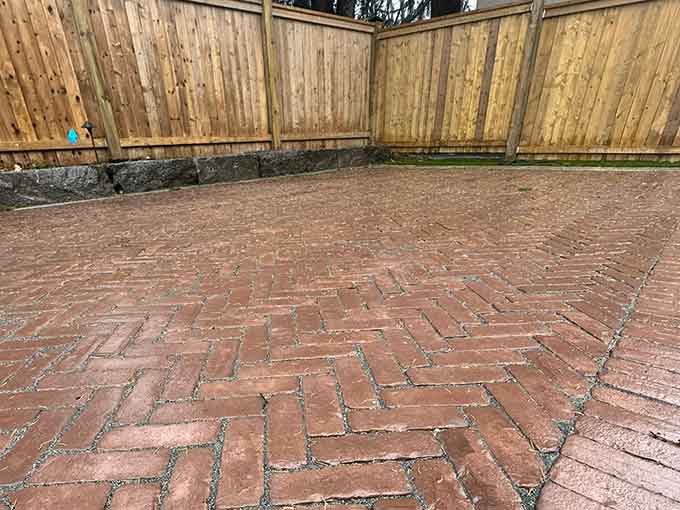 Patio with herringbone pattern pavers and wooden fence background