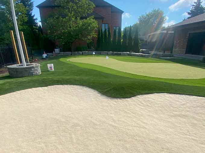 A backyard putting green with turf, sand trap, and stone edging.