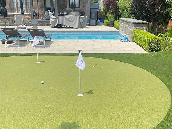 Backyard with a putting green, pool, and patio loungers.